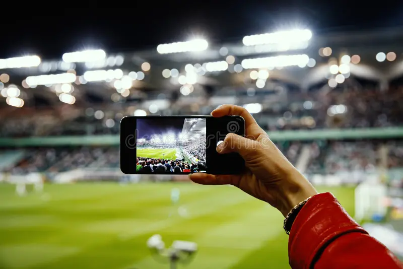 Torcedor com celular na mão gravando o jogo no estádio